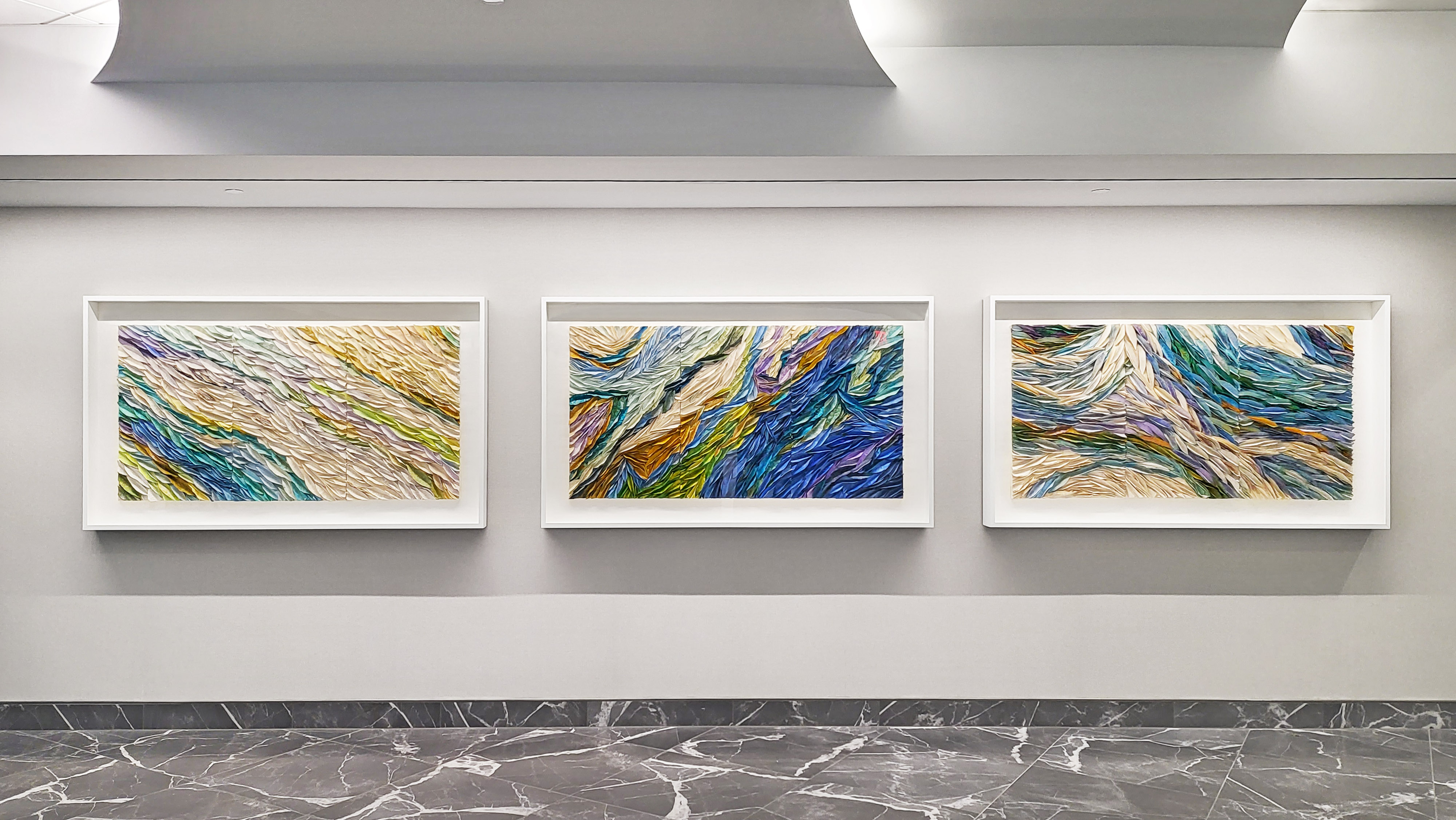 Three high quality art prints in yellows, blues, and greens hang side by sdie in thick white frames.