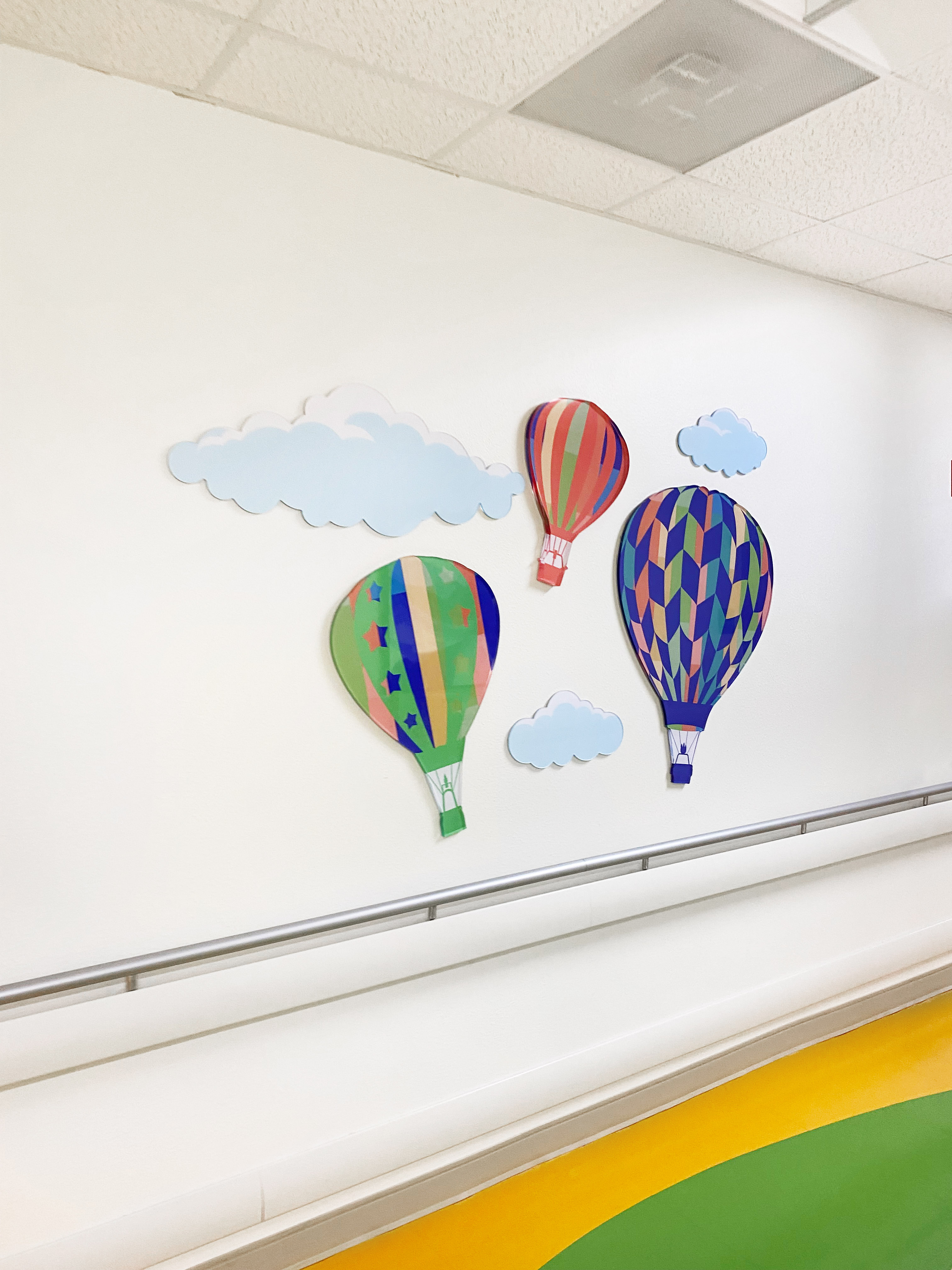 Three colorful hot air balloons and clouds installed in a hospital hallway